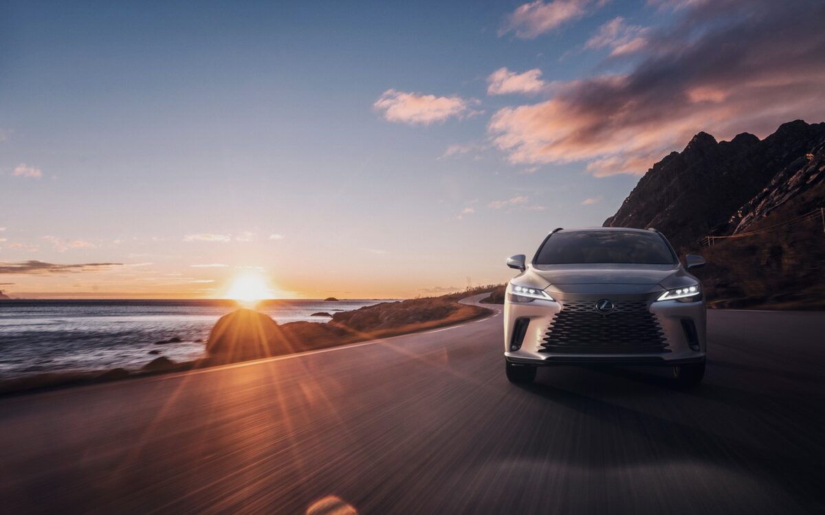 Lexus RX driving towards the camera on a coastal road at sunset