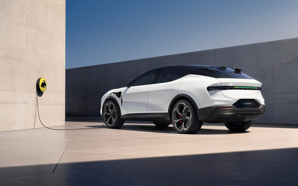 Lotus Eletre in white, rear three-quarter view charging beside a concrete wall