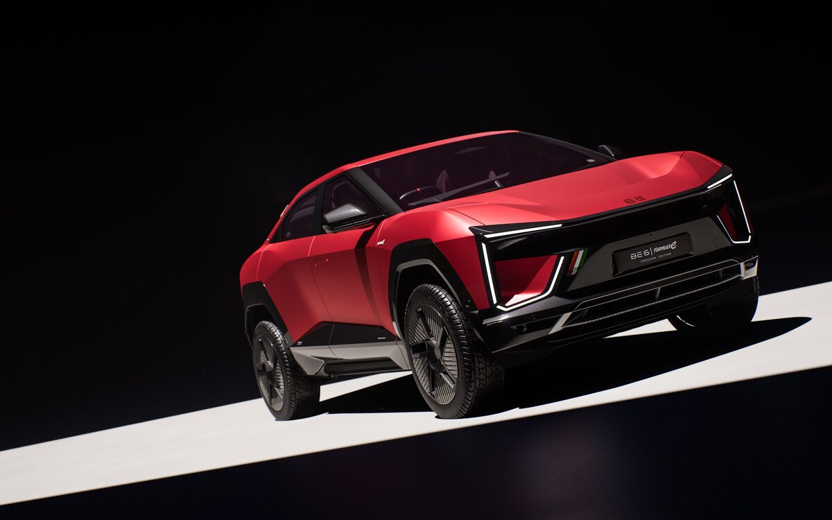 Mahindra BE 6 in red on a dark studio floor with a strip of light, front three-quarter view showing the light-bar headlamp