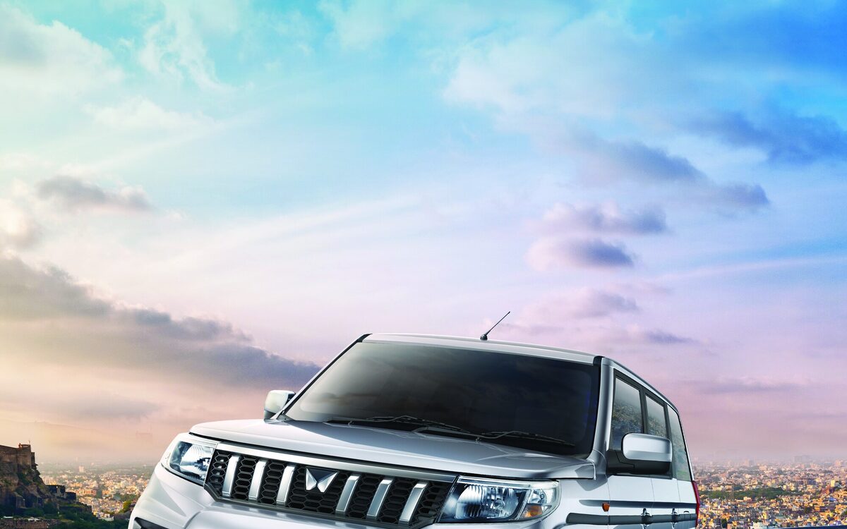 Mahindra Bolero Neo Plus in silver driving on a city road under a blue sky, front three-quarter view