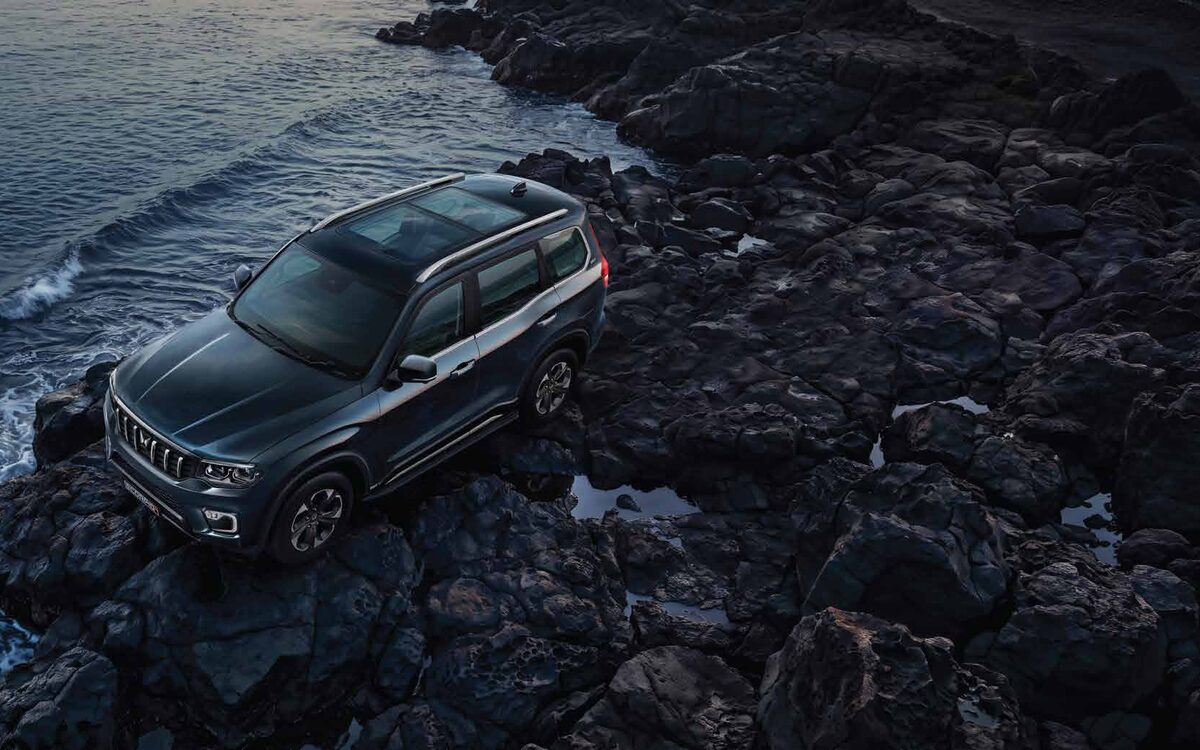 Mahindra Scorpio N parked on dark rocks by the sea, seen from above