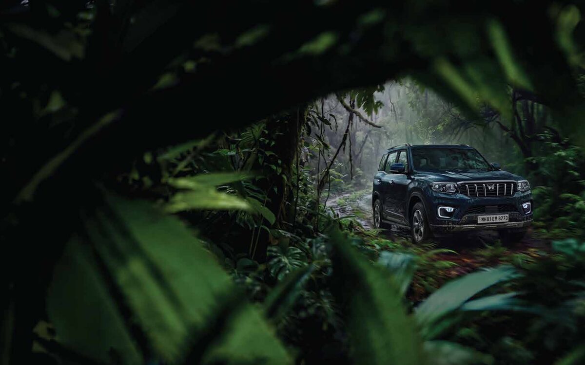 Mahindra Scorpio N driving along a trail surrounded by dense green leaves