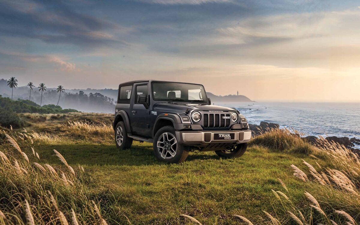 Mahindra Thar in grey parked on a grassy coastal cliff at sunset, front three-quarter view