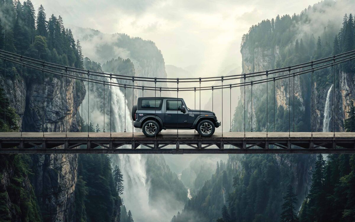Mahindra Thar in grey crossing a suspension bridge over a misty waterfall gorge, side profile