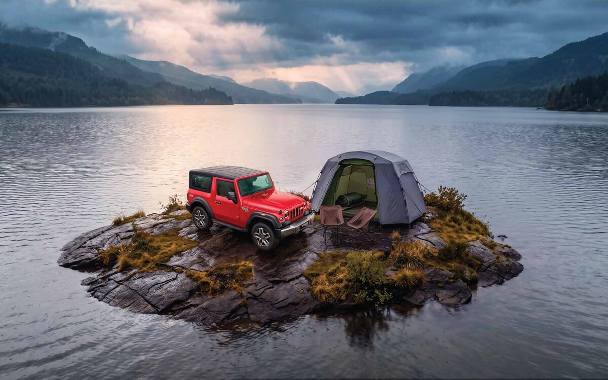 Mahindra Thar in red parked on a rocky islet in a lake next to a camping tent