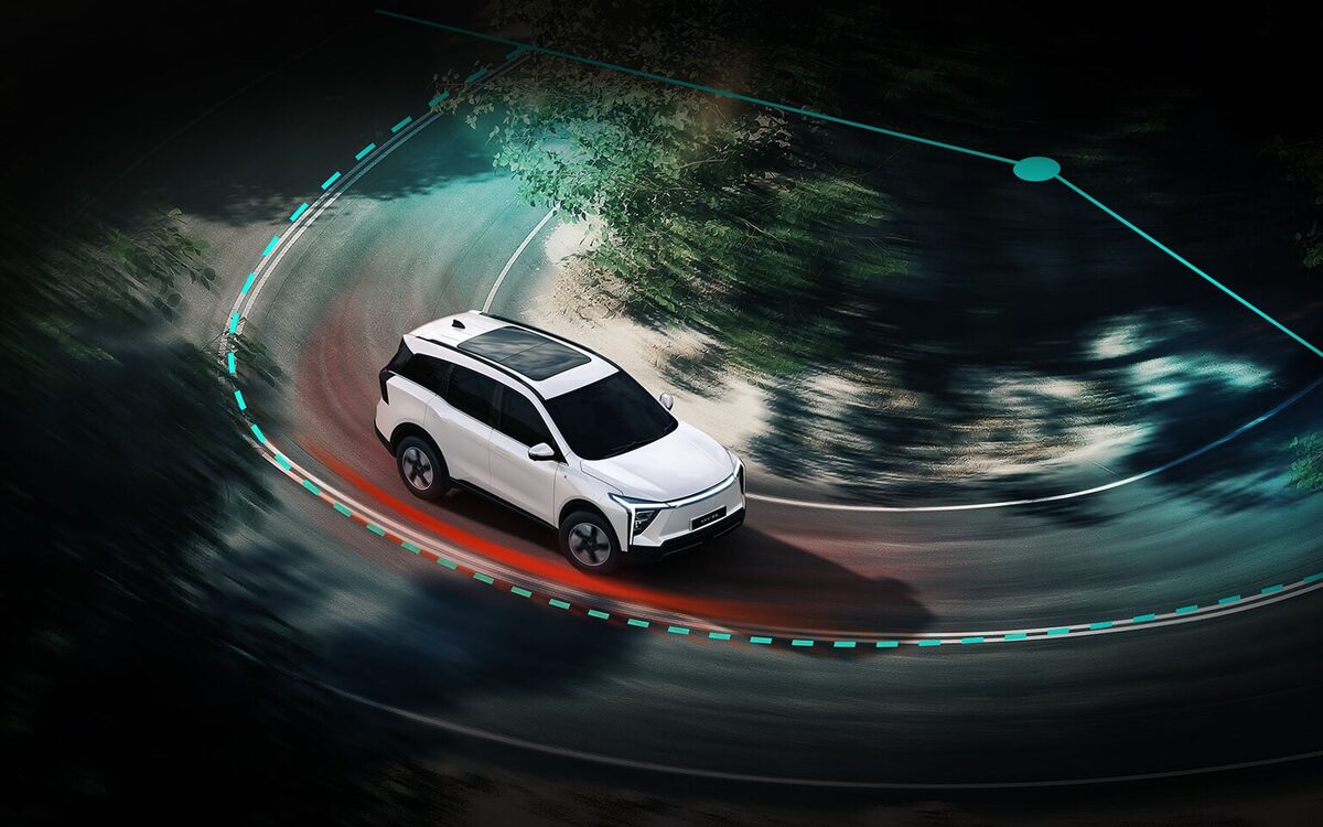 Mahindra XEV 9S in white seen from above taking a tight curve on a forest road
