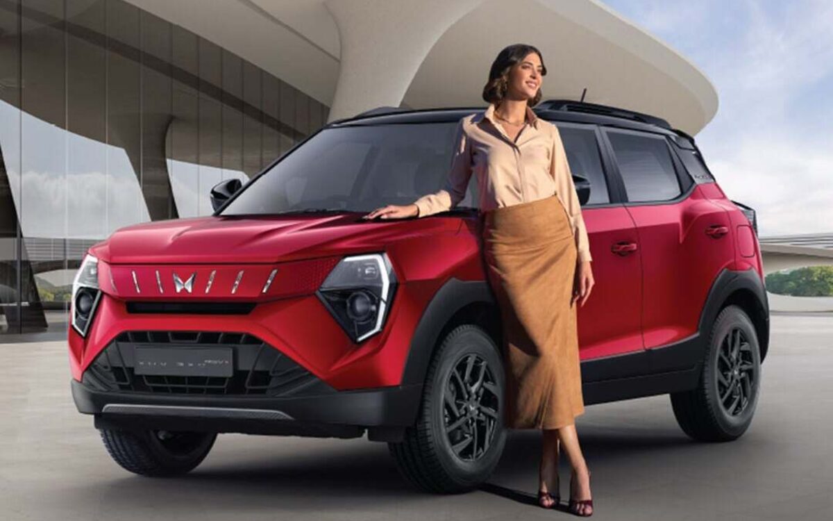 Red Mahindra XUV 3XO with a woman leaning on the bonnet, front three-quarter view outside a modern building