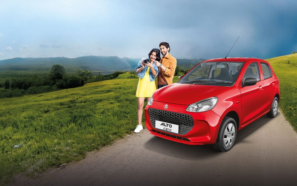 Alto K10 in red parked on a country road with two people beside it