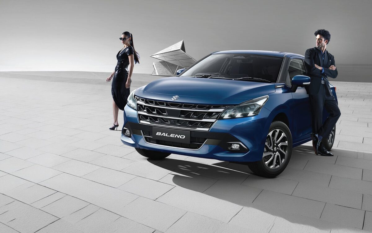 Baleno in blue, front three-quarter view with two models on a paved plaza