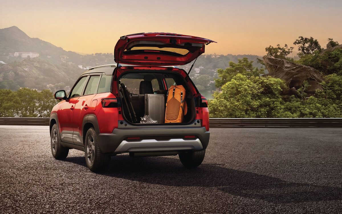 Red Brezza parked on a hilltop road at sunset with the tailgate open and luggage in the boot