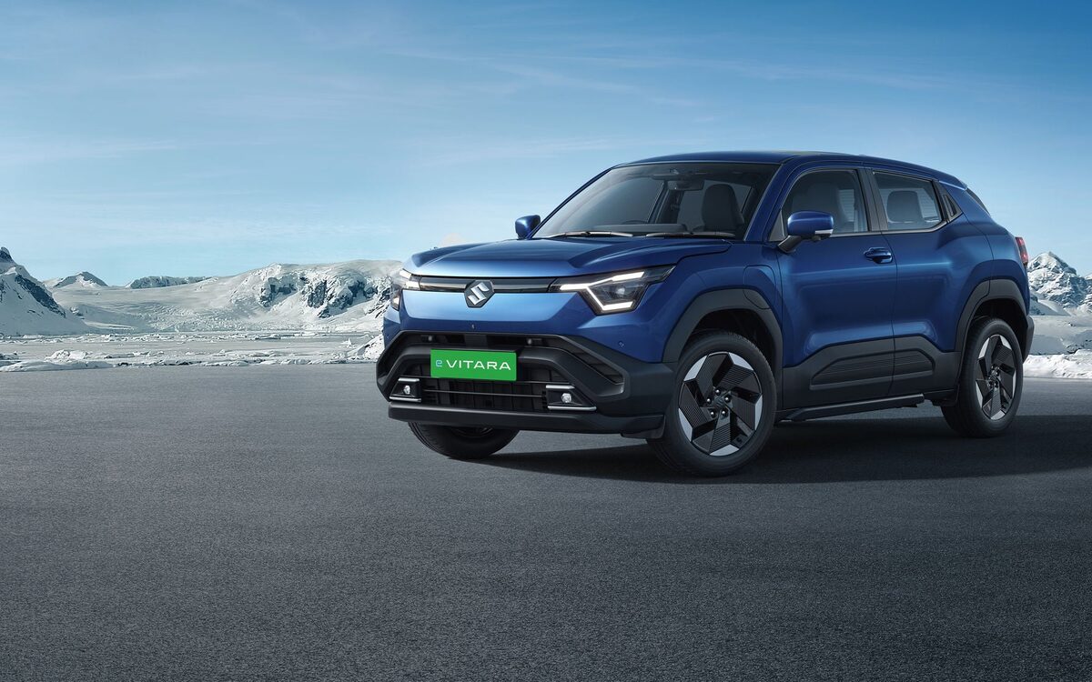 Maruti Suzuki e Vitara in blue, front three-quarter view parked on a wide road with snowy hills behind