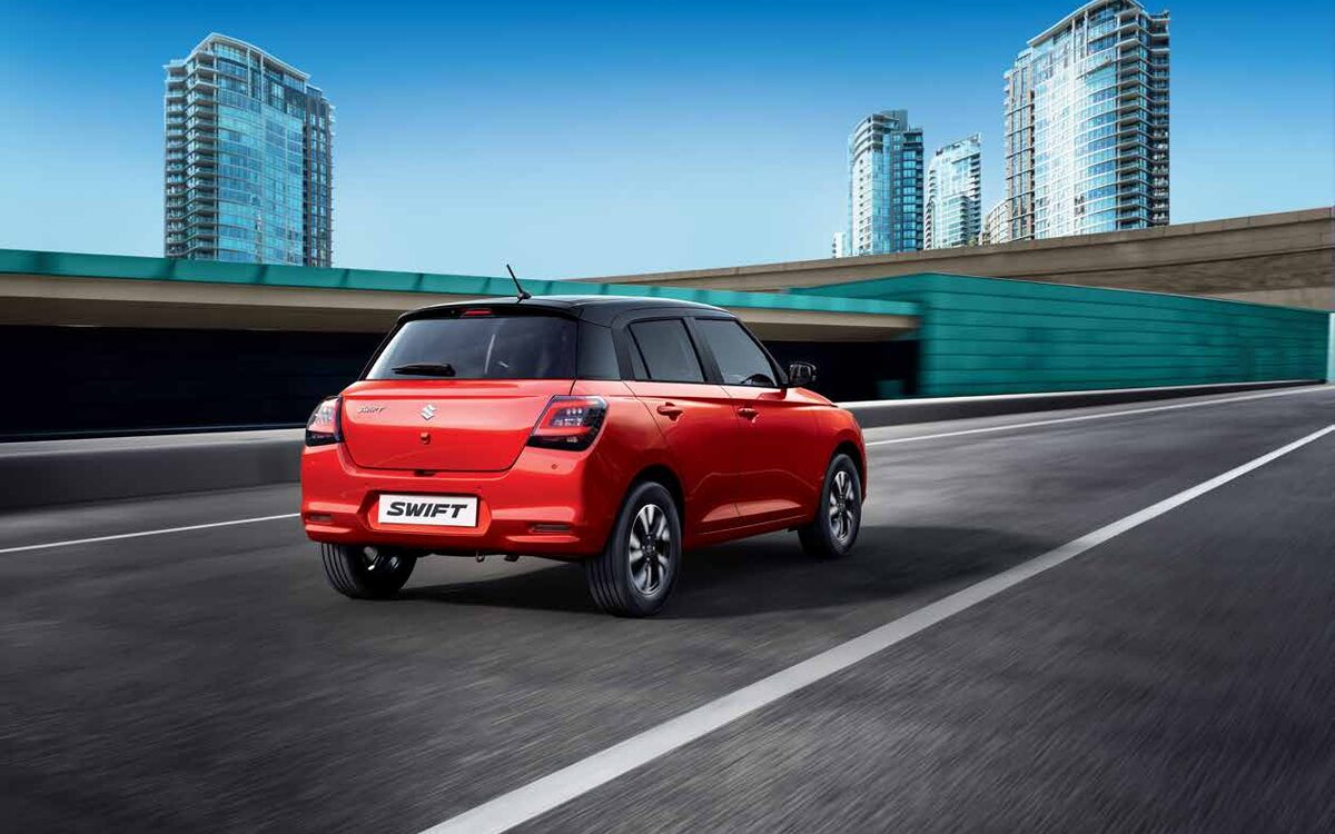 Maruti Suzuki Swift in red on a city road, rear three-quarter view