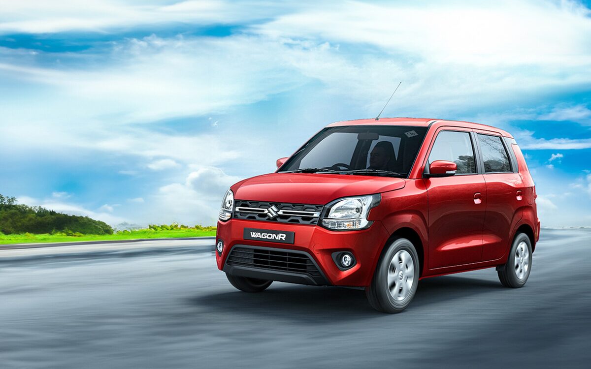 Maruti Suzuki Wagon R in red driving on a road under a blue sky with clouds, front three-quarter view