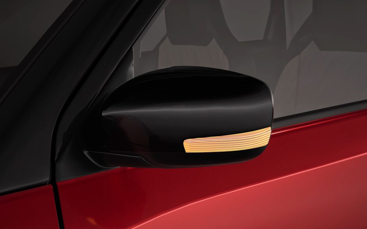 Close-up of the Wagon R's black door mirror with built-in orange turn indicator on a red door