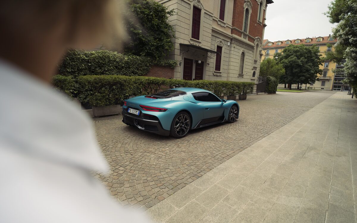 Teal Maserati MCPURA parked on a city street with a man looking on