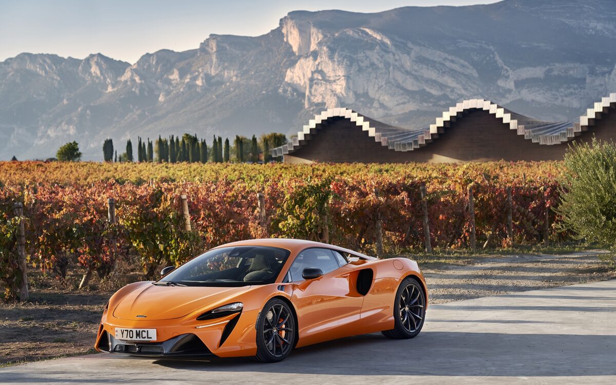 McLaren Artura in orange, front three-quarter view in front of a vineyard and mountains