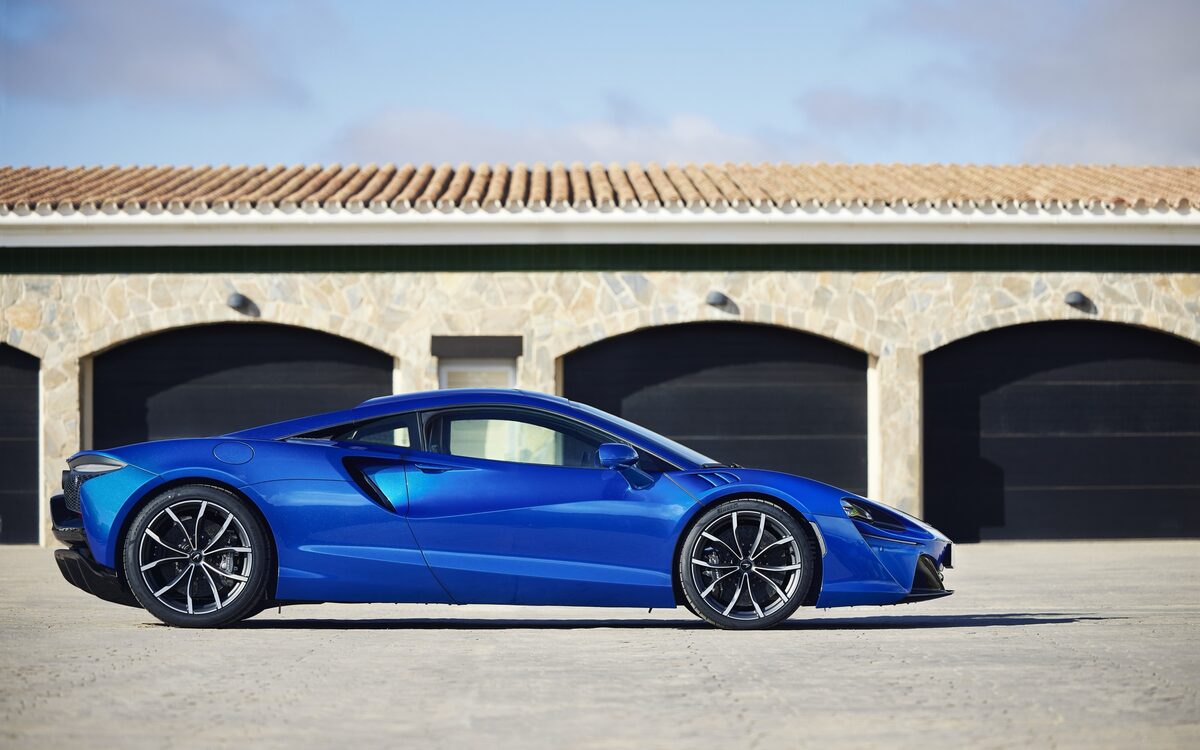 McLaren Artura in blue, parked side profile in front of garage doors