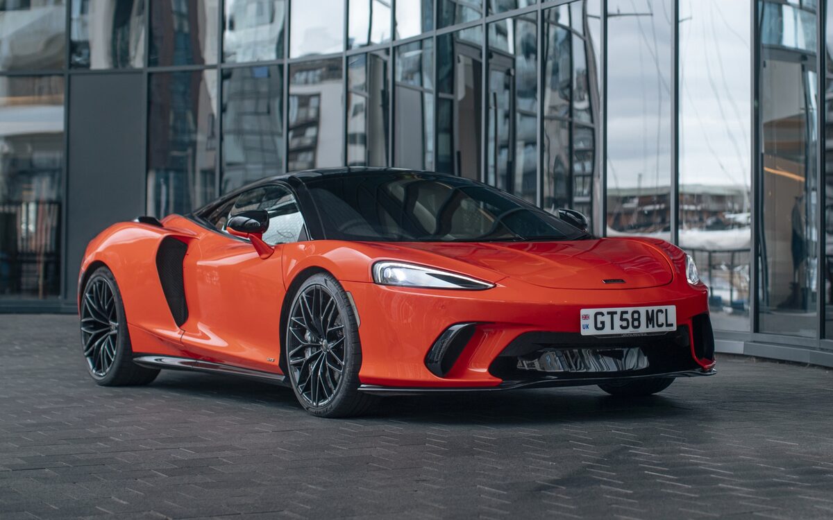 McLaren GTS in orange, front three-quarter view in front of a glass building