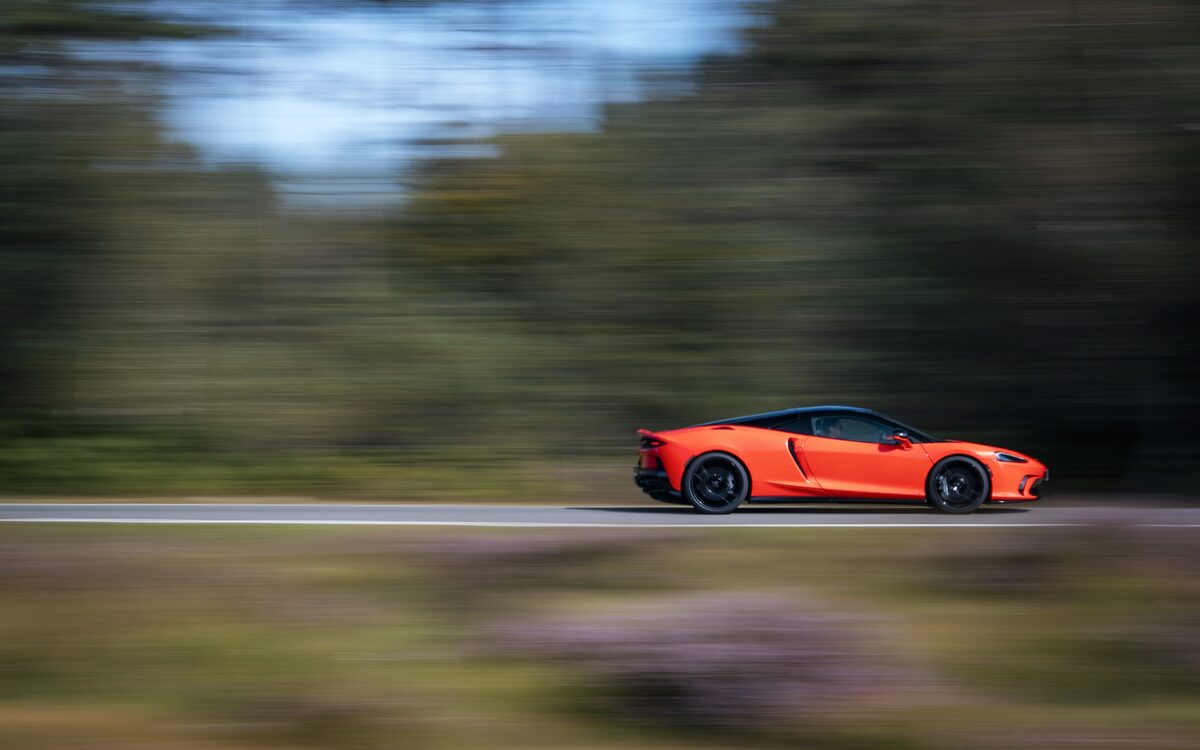 McLaren GTS in orange driving past blurred trees in side profile