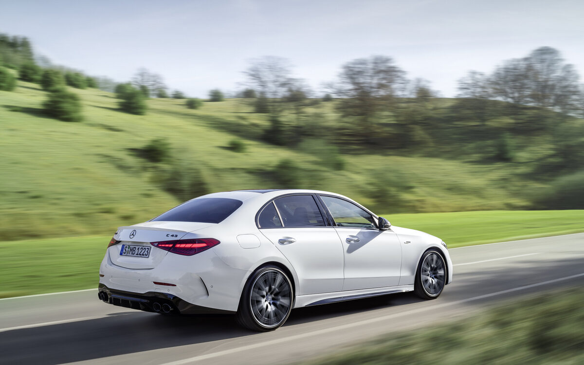 Mercedes-AMG C 43 in Opalite White driving on a country road, rear three-quarter view