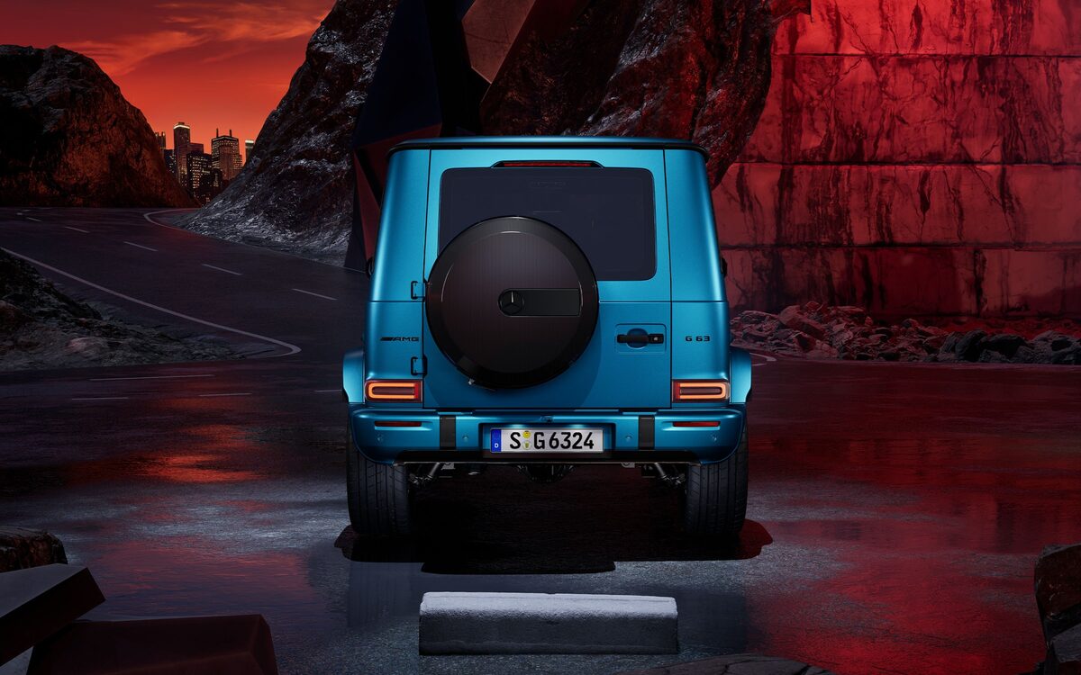 Mercedes-AMG G 63 in bright blue seen from behind on a rocky road at night, spare wheel cover and AMG number plate visible