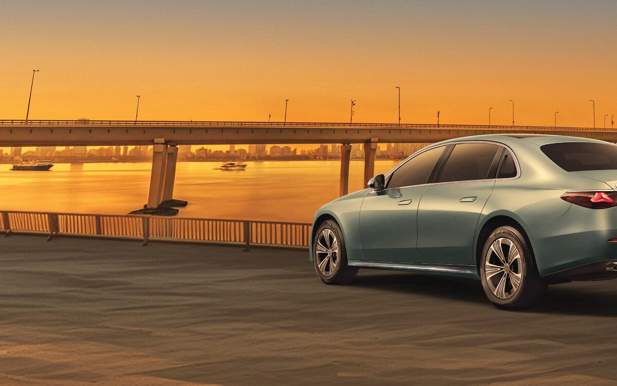 E-Class LWB in Verde Silver parked beside a bridge at sunset, rear three-quarter view