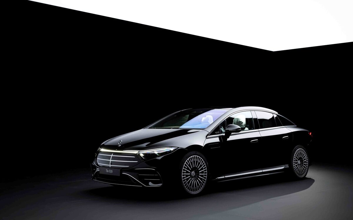 Mercedes-Benz EQS 580 in black, front three-quarter view in a dark studio with the illuminated grille
