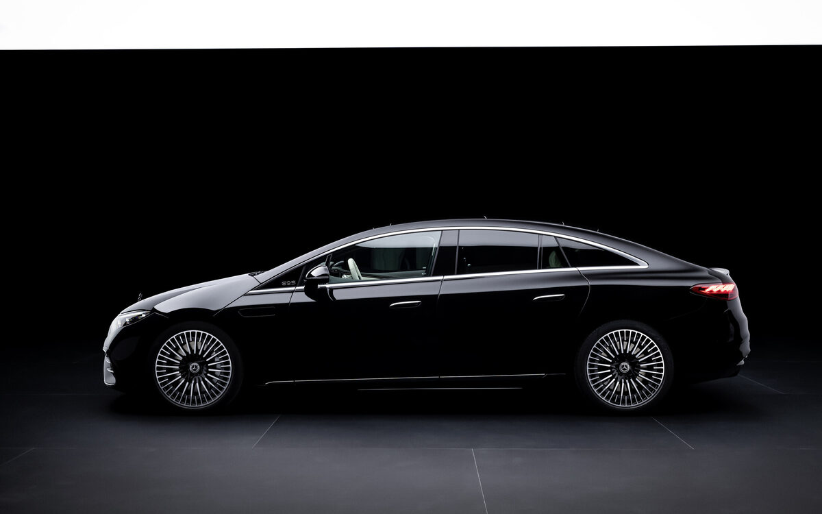 Mercedes-Benz EQS saloon in black seen from the side in a dark studio, showing its long sloping roofline and aero wheels