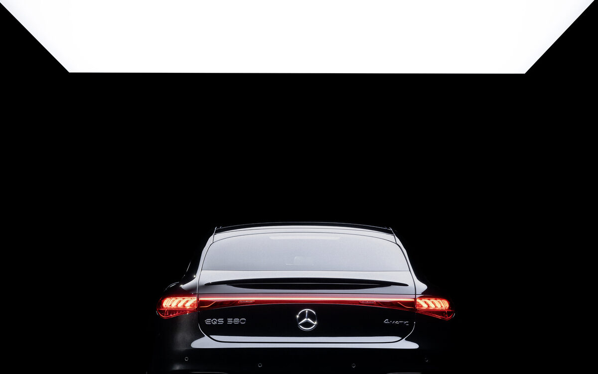 Mercedes-Benz EQS 580 seen from directly behind in a dark studio with the full-width red tail light bar