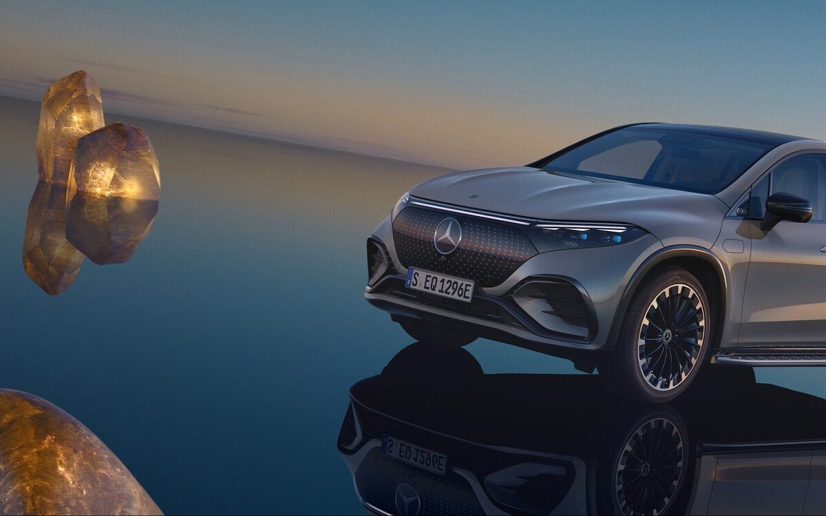 EQS SUV in grey, front three-quarter view, parked on a mirror-like surface at dusk