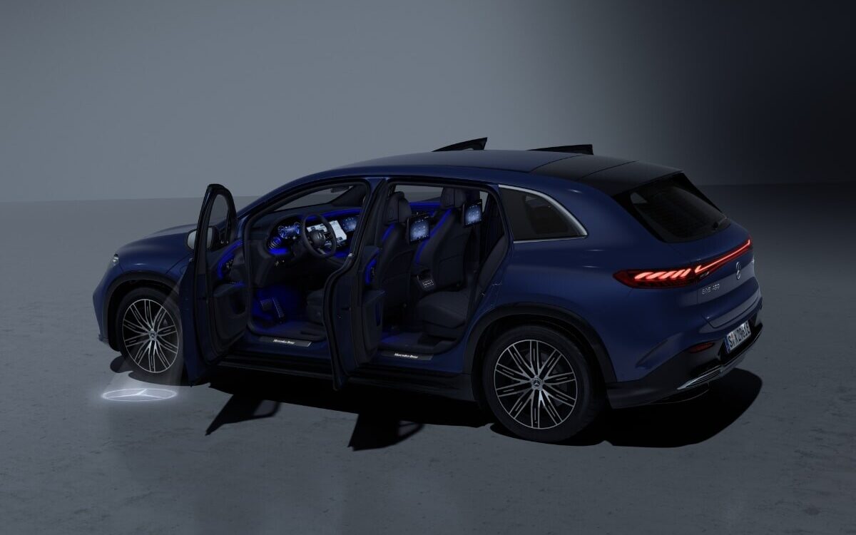 Blue EQS SUV in a dark studio with all doors open showing the lit cabin and a star projection on the floor