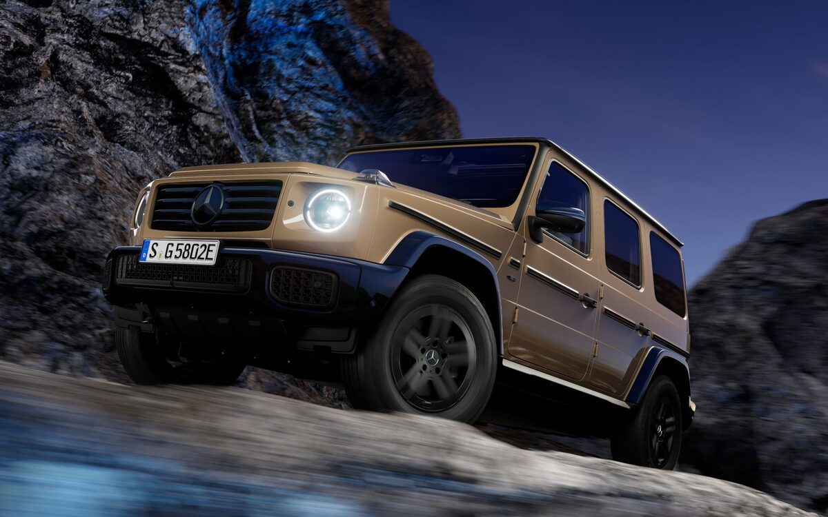 Mercedes-Benz G 580 with EQ Technology in a sand-gold paint climbing a rocky slope at dusk, front three-quarter view with headlamp lit