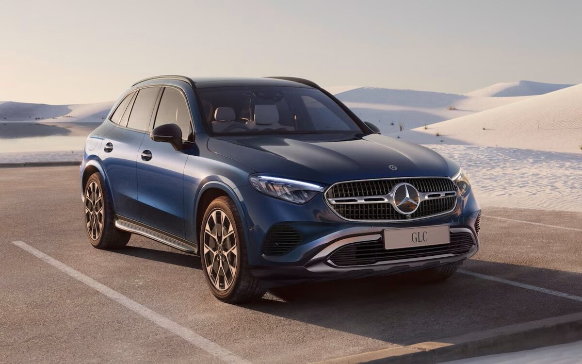 Mercedes-Benz GLC in blue, front three-quarter view parked on a sandy lot with dunes behind