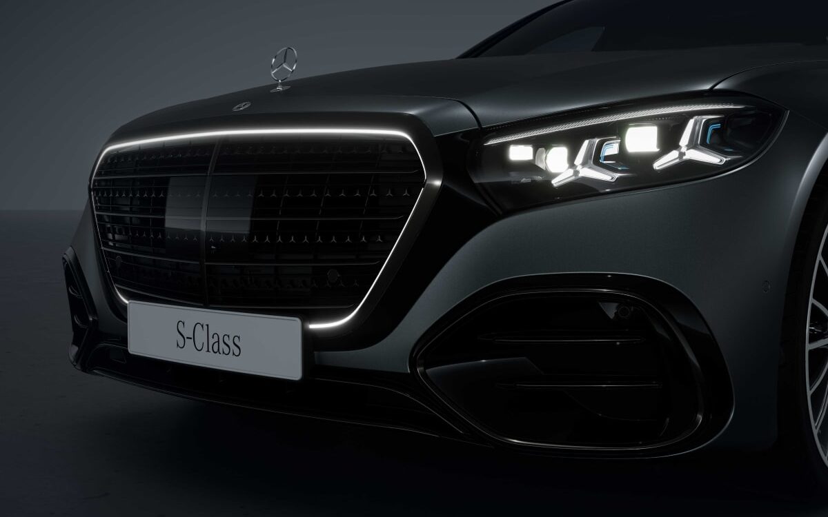 Front of a dark Mercedes-Benz S-Class showing the large grille with its lit surround, bonnet star and headlamp