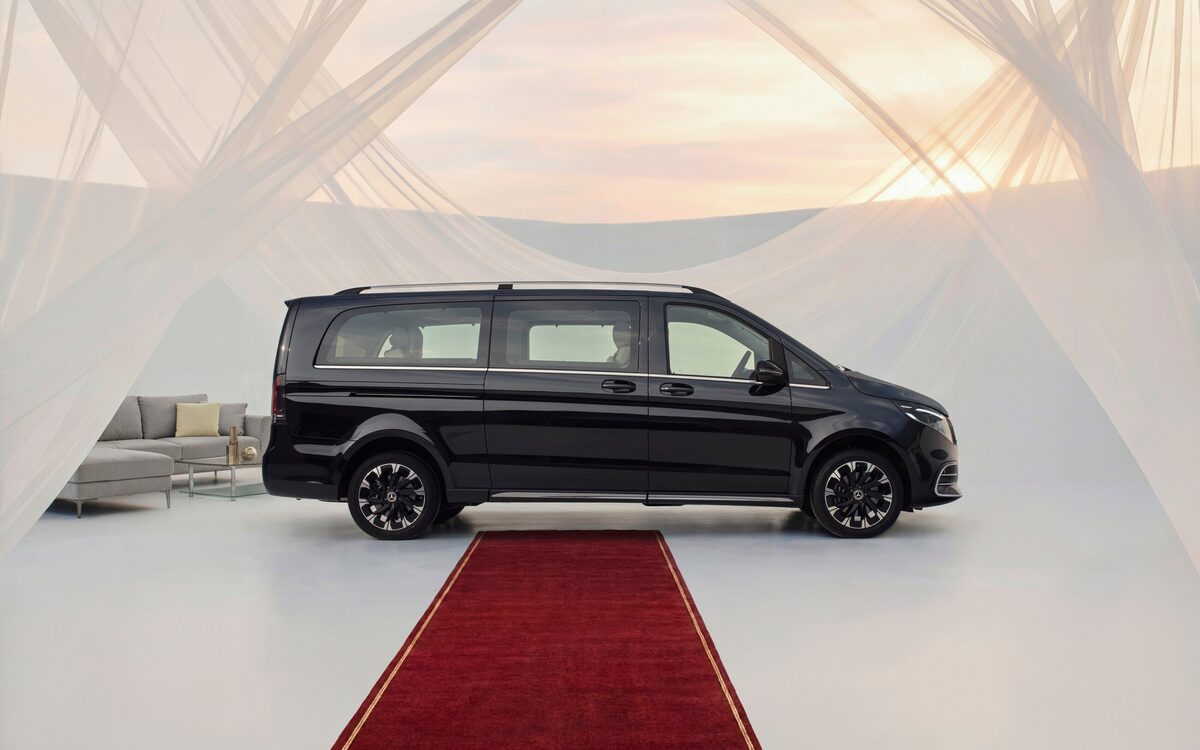 Black Mercedes-Benz V-Class in side profile on a white stage with a red carpet and sheer curtains