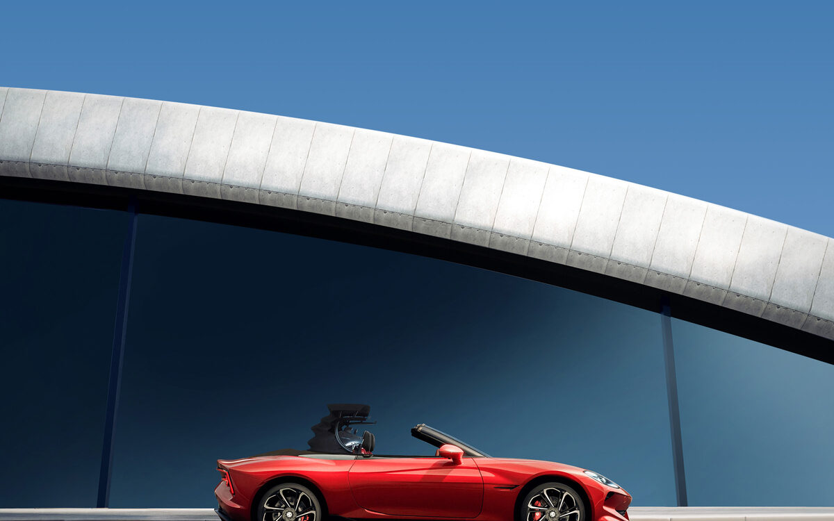 MG Cyberster in red with the roof open, side profile on a road in front of a curved building