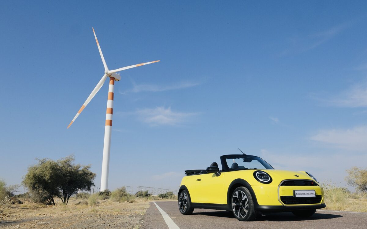 Yellow MINI Convertible with the roof down on a road beside a wind turbine