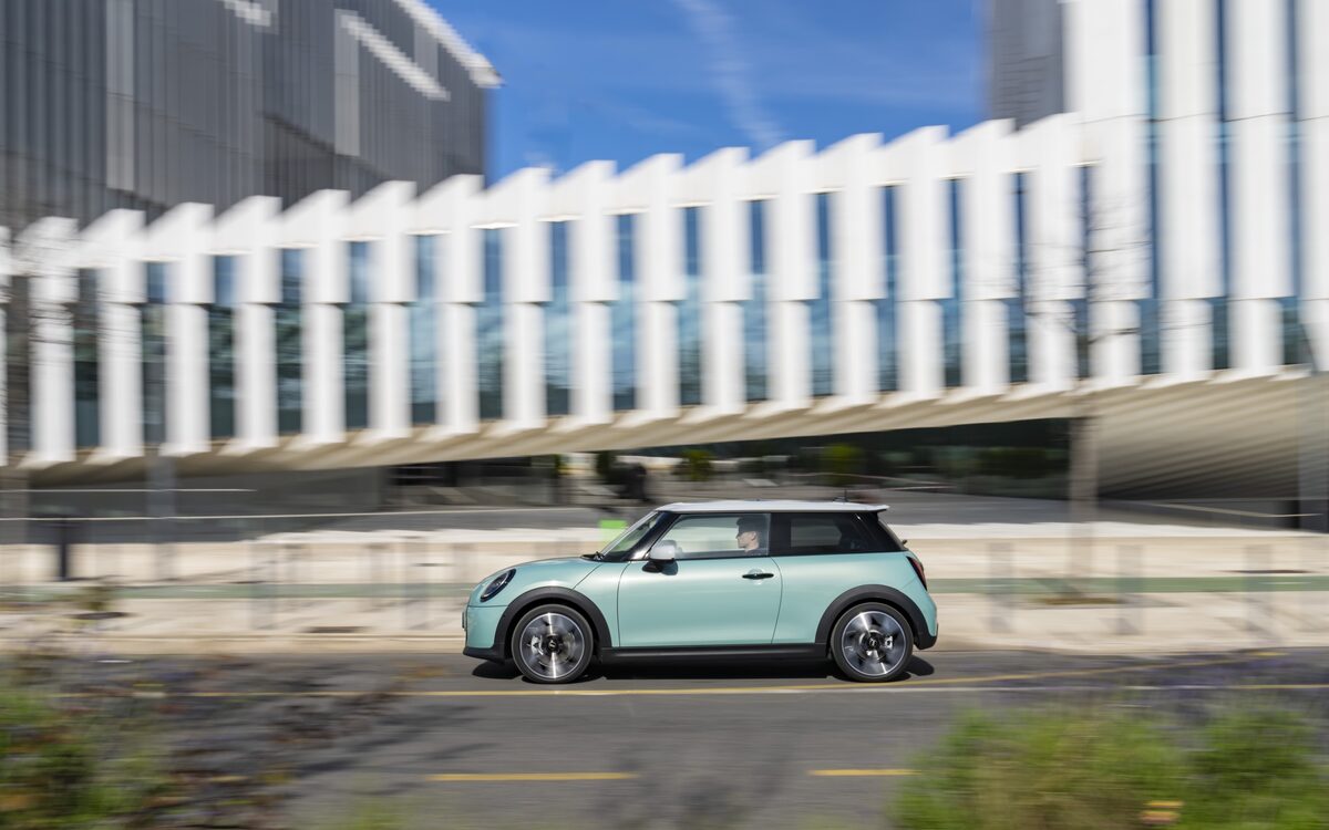 MINI Cooper S three-door in light green driving past a modern building, side profile