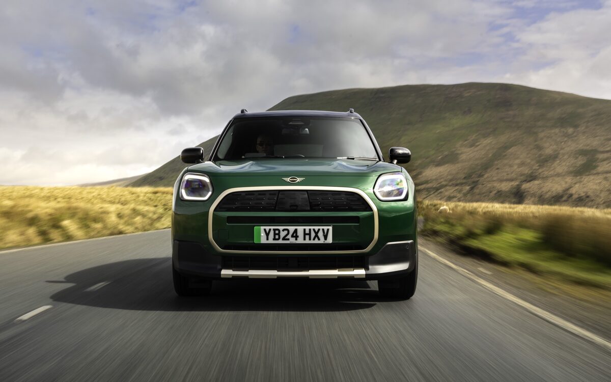 MINI Countryman Electric in green driving towards the camera on a hilly road