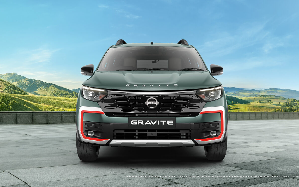 Nissan Gravite in Forest Green, front view on a paved plaza with green hills behind