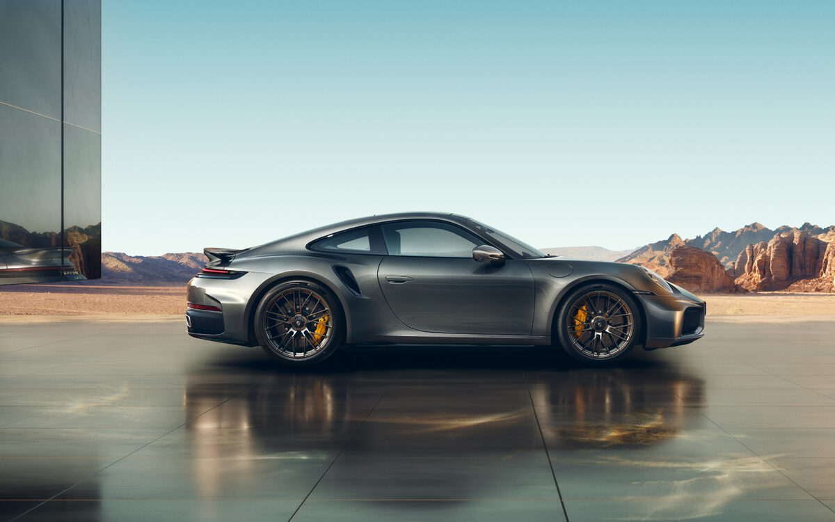Porsche 911 Turbo S in grey, side profile on a stone plaza in front of desert rocks