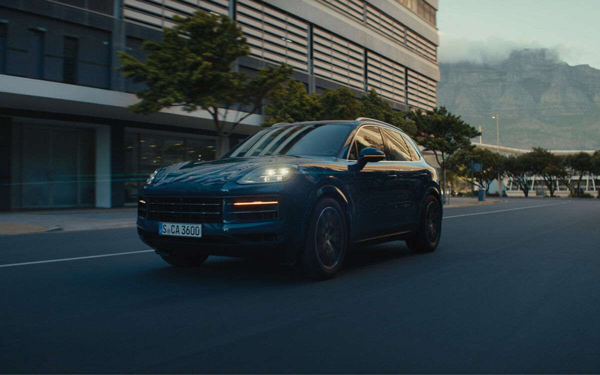 Porsche Cayenne in blue driving towards the camera at dusk with its headlamps on
