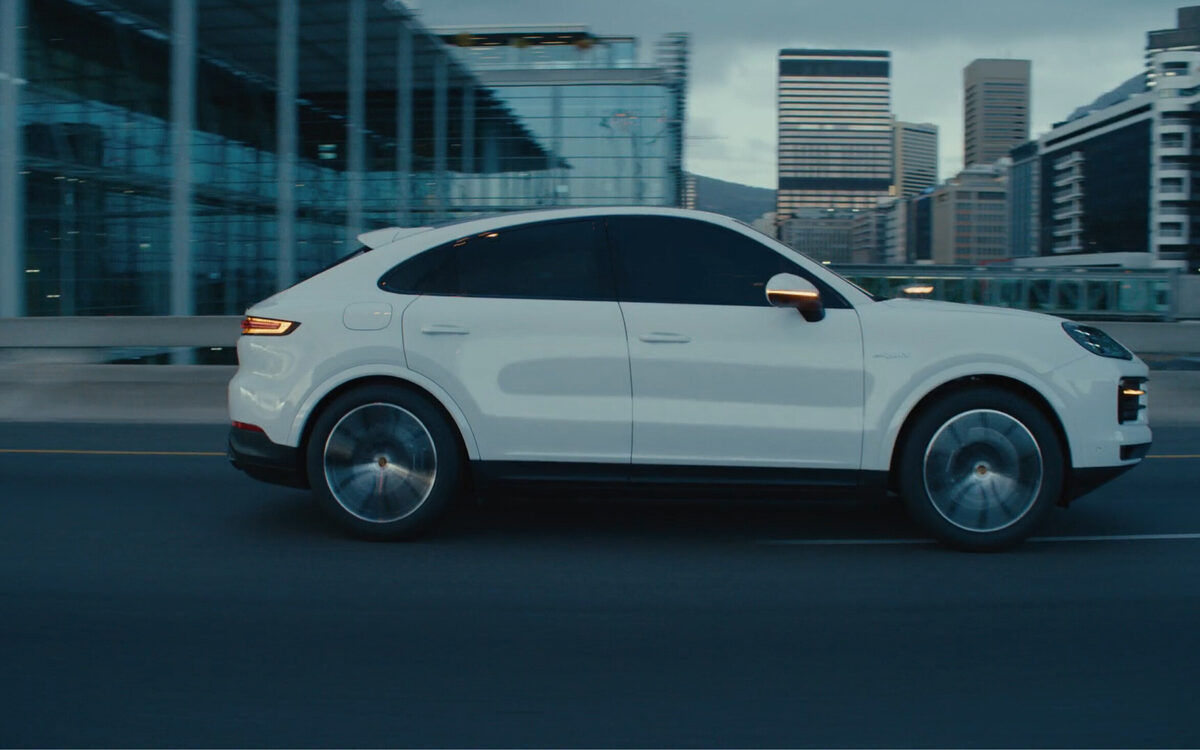 White Porsche Cayenne Coupe driving past glass office buildings