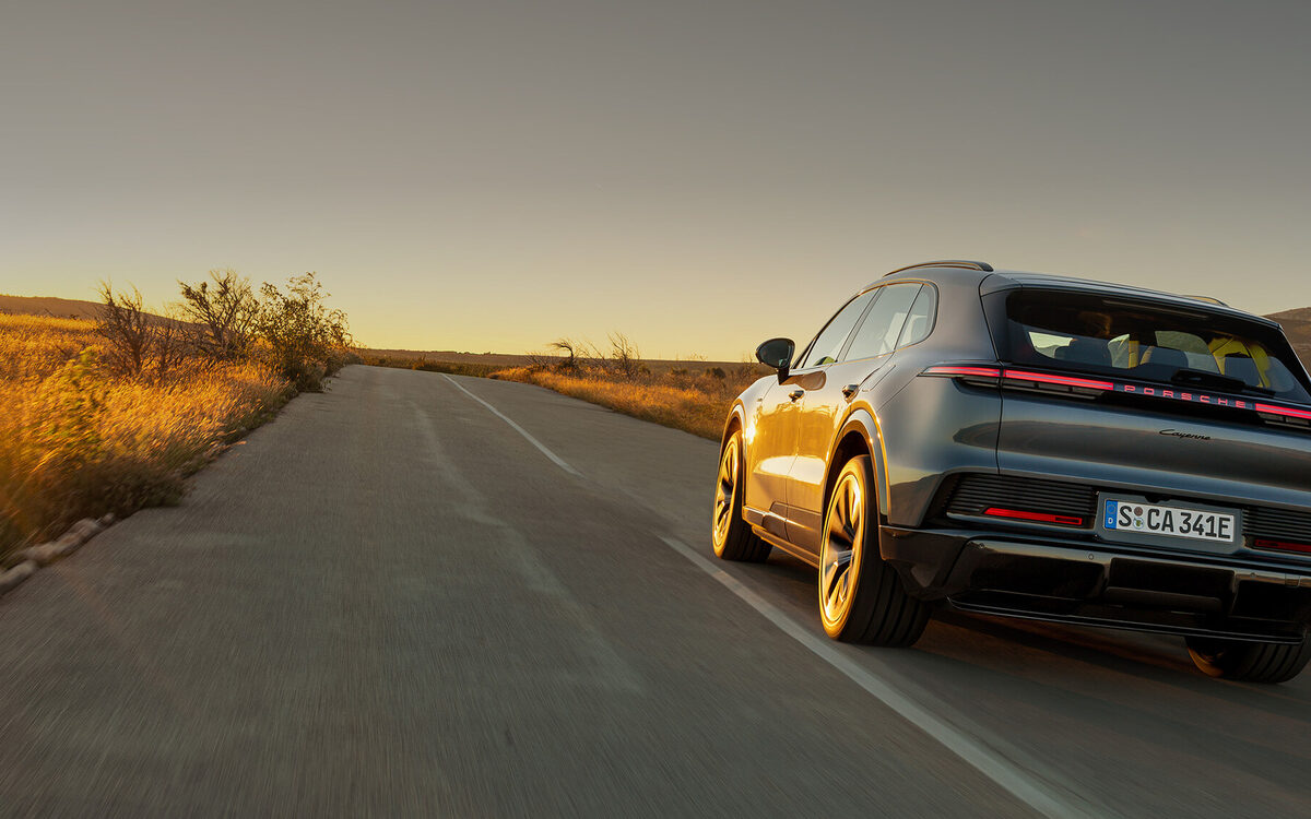 Porsche Cayenne Electric driving along an empty road at sunset, seen from behind