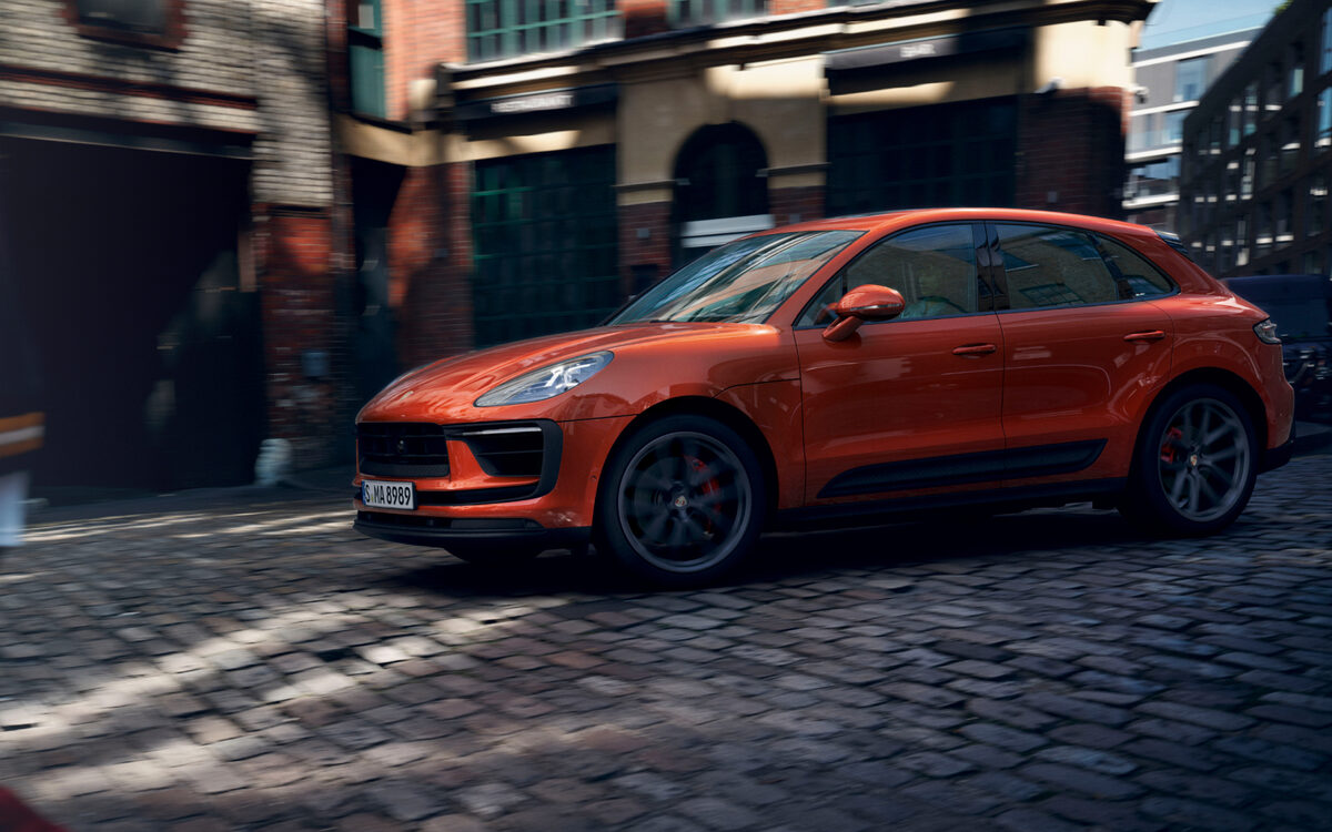 Orange Porsche Macan driving along a cobbled street