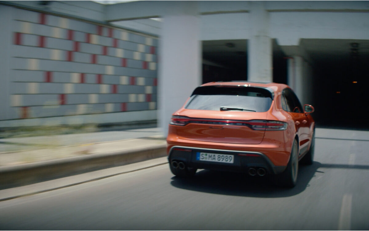 Orange Porsche Macan driving away through a car park