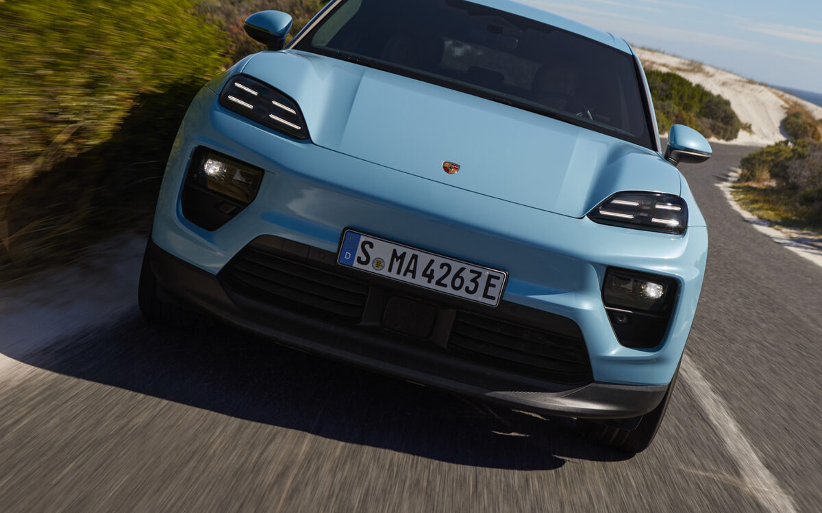 Light blue Porsche Macan Electric driving towards the camera on a coastal road