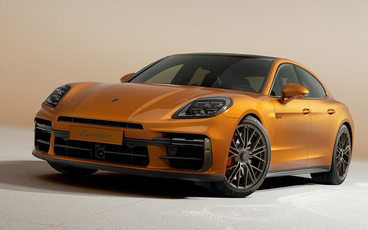 Porsche Panamera in orange, front three-quarter view in a sunlit studio