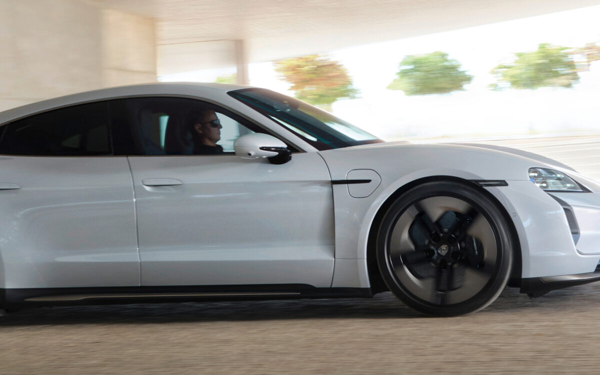 Silver Porsche Taycan driving past under a concrete overpass