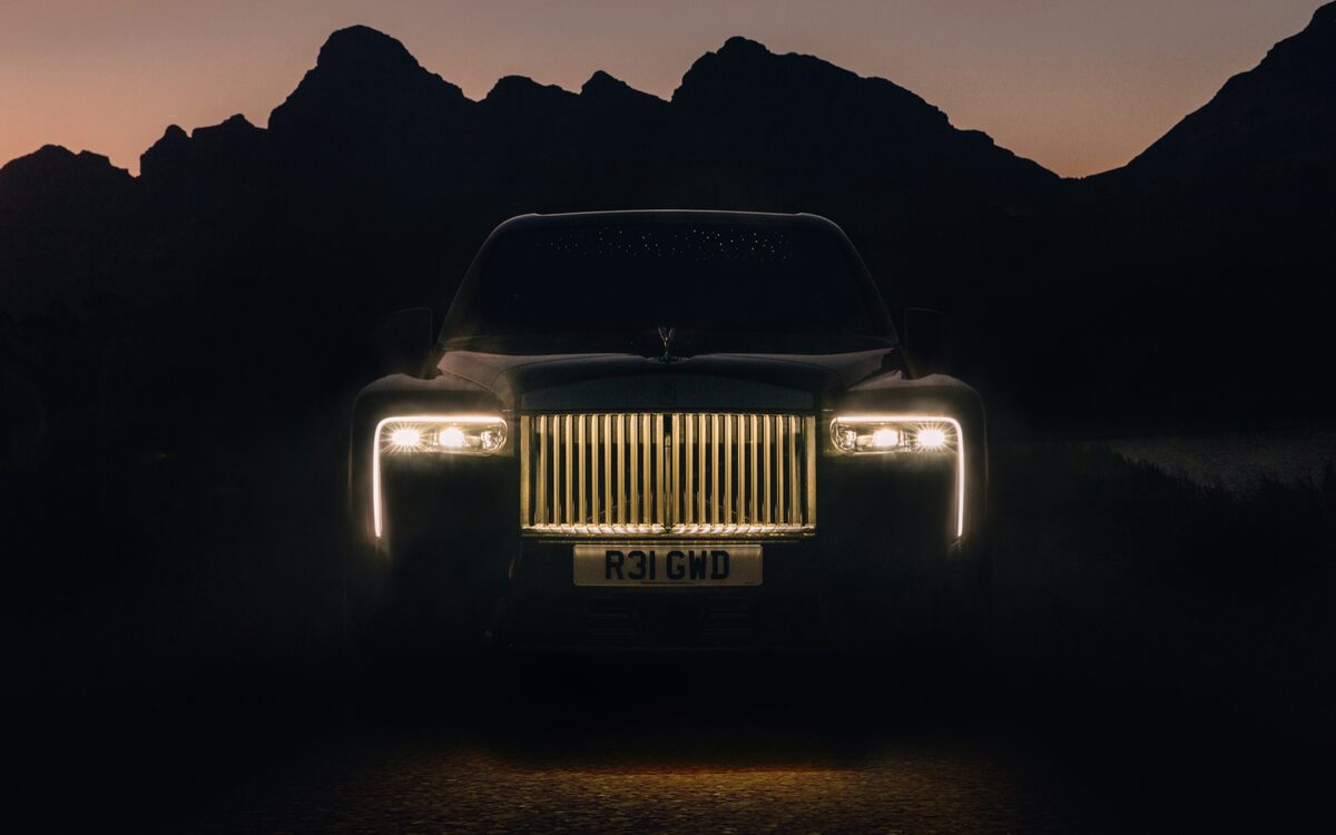 Rolls-Royce Cullinan from the front at dusk with illuminated grille and light signature, mountains behind